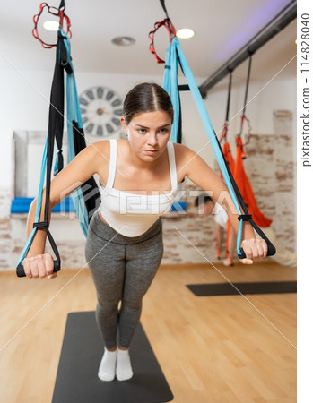 Sporty girl doing push-ups using TRX suspension straps during Pilates workout 114828040