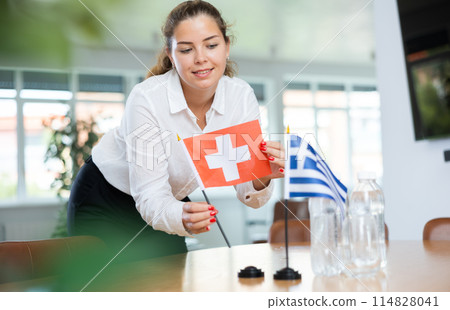 Young female secretary preparing room for international negotiations between greece and switzerland 114828041
