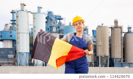National flag of Belgium in the hands of girl in overalls against background of modern metallurgical plant National flag of Belgium in the hands of girl in overalls against background of modern metallurgical plant 114828070