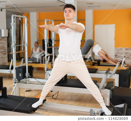 Guy performing exercises on Pilates reformer to stretch body muscles 114828089