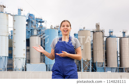 Happy young woman worker posing against background of factory Happy young woman worker posing against background of factory 114828111