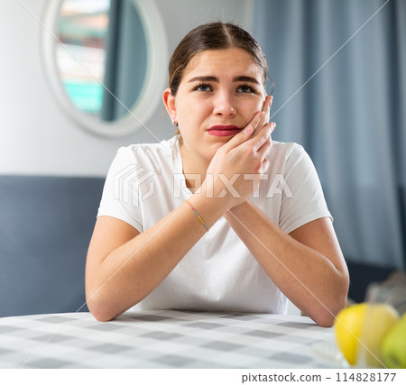 Sick woman experiencing severe pain in tooth while sitting at table Sick woman experiencing severe pain in tooth while sitting at table 114828177
