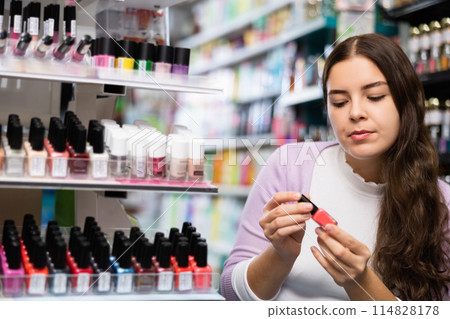 Cheerful pretty woman customer holding nail varnish bottles in boutique 114828178