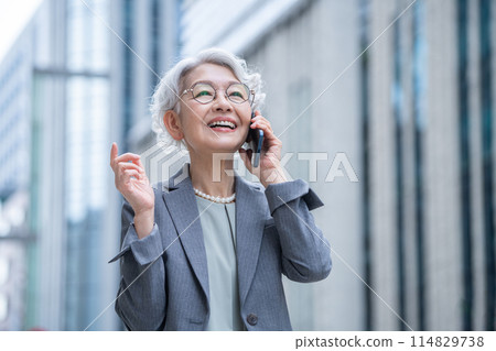 Senior woman holding a smartphone in an office district Senior woman holding a smartphone in an office district 114829738