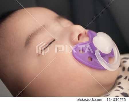 A baby sleeping peacefully in a stroller with a pacifier A baby sleeping peacefully in a stroller with a pacifier 114830753