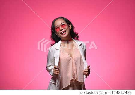 Portrait of a cheerful middle aged woman with fashionable outfit posing over pink background Portrait of a cheerful middle aged woman with fashionable outfit posing over pink background 114832475