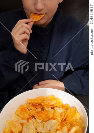 Caucasian person in navy blue t-shirt holding plate full of potato chips, young male eating potato chips 114834657