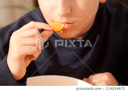 Caucasian person in navy blue t-shirt holding plate full of potato chips, young male eating potato chips Caucasian person in navy blue t-shirt holding plate full of potato chips, young male eating potato chips 114834672