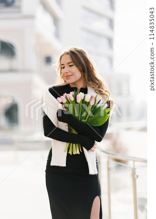 Young woman is distracted from her daily routine, enjoying the beauty of tulips, walking around the city 114835043