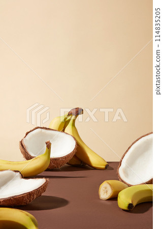 Vertical photo was taken from front with light yellow background, brown color table top containing plenty coconut and banana with empty space in the middle. Space for designing and adding text 114835205