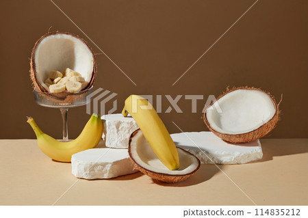 A few empty plaster podiums are placed on a yellow table top with bananas and coconuts scattered decorated around against brown background. Front view photo, displaying space A few empty plaster podiums are placed on a yellow table top with bananas and coconuts scattered decorated around against brown background. Front view photo, displaying space 114835212