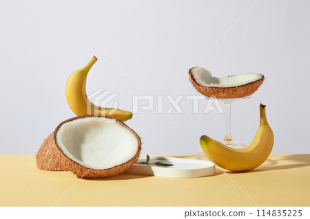 Several fresh fruits consist of yellow banana and coconut featured on yellow table top against white background, white empty tray for showing product and copy space for adding text 114835225