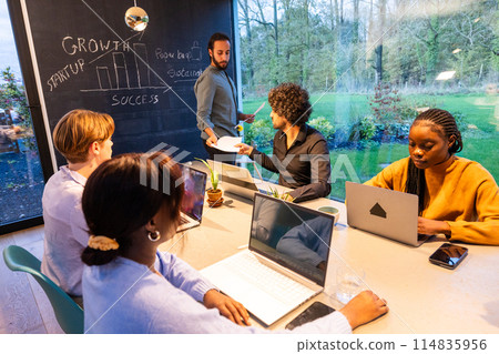 A group of individuals sitting around a table, each with a laptop 114835956