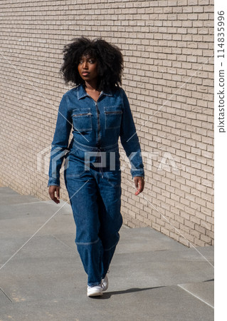 Black Woman Walking Outdoors in Denim Jumpsuit 114835996