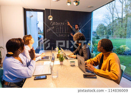 A group of people are at a table talking and using laptops A group of people are at a table talking and using laptops 114836009