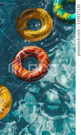 Aerial view of a sunlit pool with colorful inflatable swim rings on the water's surface 114837136