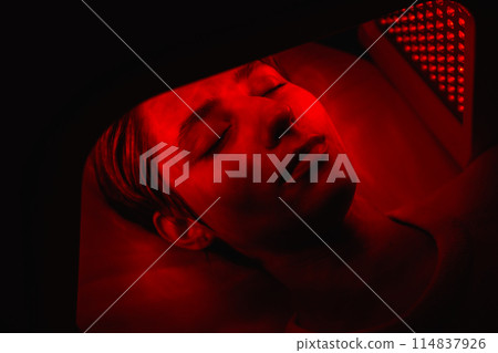 A young woman is treating the skin of her face with the help of LED light. A young woman is treating the skin of her face with the help of LED light. 114837926