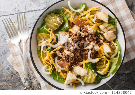 Homemade Cheeseburger Salad with lettuce, ground beef, pickles, cheddar cheese, onions and dressed with spicy sauce closeup on the bowl. Horizontal top view Homemade Cheeseburger Salad with lettuce, ground beef, pickles, cheddar cheese, onions and dressed with spicy sauce closeup on the bowl. Horizontal top view 114838042