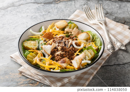 Homemade Cheeseburger Salad with lettuce, ground beef, pickles, cheddar cheese, onions and dressed with spicy sauce closeup on the bowl. Horizontal 114838050