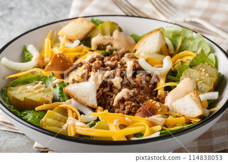 American Cheeseburger Salad with romaine lettuce, ground beef, pickles, cheddar cheese, onions and dressed with a special burger sauce closeup on the bowl. Horizontal American Cheeseburger Salad with romaine lettuce, ground beef, pickles, cheddar cheese, onions and dressed with a special burger sauce closeup on the bowl. Horizontal 114838053