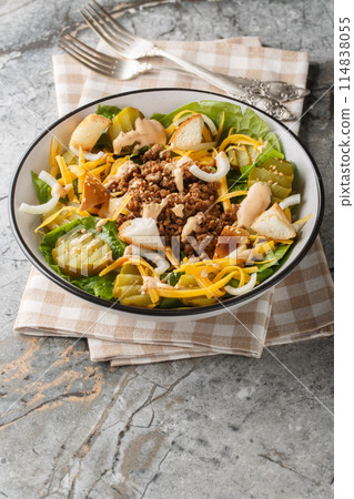 Cheeseburger salad with romaine lettuce, ground beef, pickles, cheddar cheese and croutons close-up in a bowl. Vertical 114838055
