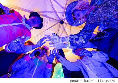 Attendees dressed in costumes having a great time amidst colorful lights at a lively celebration 114839870