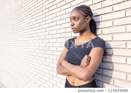 A thoughtful young woman with braided hair leaning against a brick wall in an urban setting A thoughtful young woman with braided hair leaning against a brick wall in an urban setting 114839890