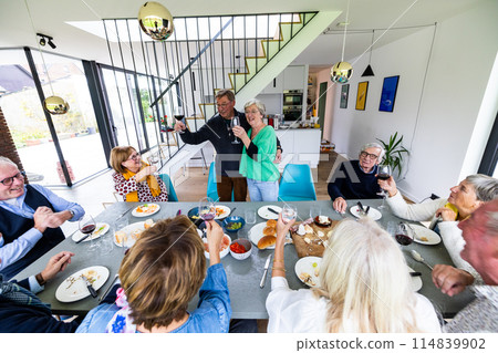 Senior friends enjoying food and drink in a modern dining room, sharing joy and happiness 114839902