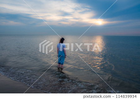 Pensive Person Gazing into the Sunset Over Calm Seas 114839934