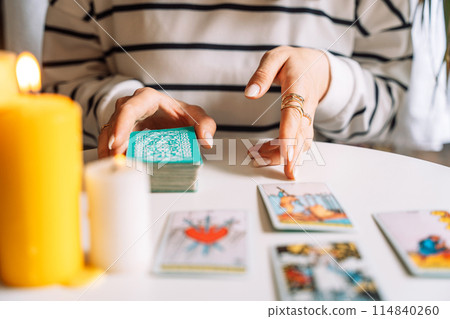 Lady tarot reader tells fortunes with tarot cards on a white table with burning candles 114840260