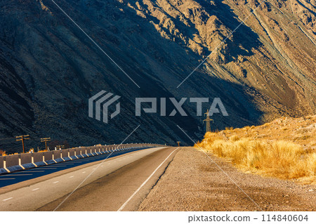Desolate asphalt thoroughfare cuts through mountainous natural landscape 114840604