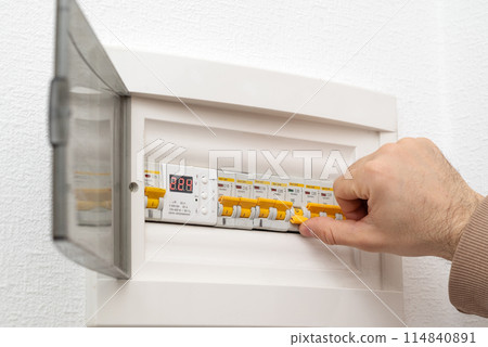 Hand is turning on circuit breaker on control panel after it tripped due to overload 114840891