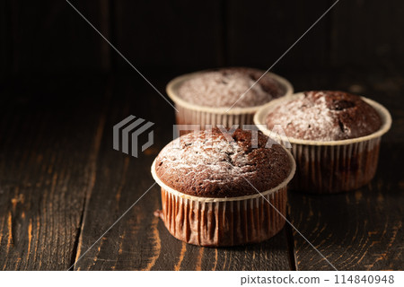 Chocolate muffins with powdered sugar on a black background. Still life close up. Dark moody. Food photo. 114840948