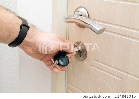The man unlocks the wooden door in modern house. man opens door with his hand. Key on the door. The man unlocks the wooden door in modern house. man opens door with his hand. Key on the door. 114841019