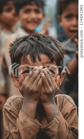 A young boy with his hands over his eyes stands out with a blurred background, engaged in a playful game. His peers await in anticipation, completing the scene. 114841965