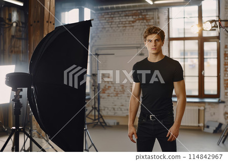 Young man in a black t-shirt posing in a photography studio. Professional photoshoot setting. 114842967