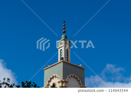 A beautiful tower of the minaret of a mosque in Morocco with square walls decorated with white, green tiles in the form of a Muslim eight-pointed star, a flower against a blue sky A beautiful tower of the minaret of a mosque in Morocco with square walls decorated with white, green tiles in the form of a Muslim eight-pointed star, a flower against a blue sky 114843544
