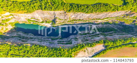 An aerial view of the abandoned limestone quarry Velka Amerika in Czechia, revealing clear, turquoise water surrounded by lush greenery and rugged rock formations. 114843793