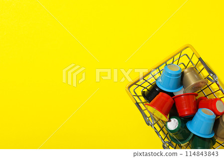 Colored coffee capsules in shopping basket on yellow background, space for text 114843843
