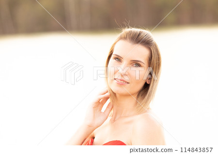 A woman wearing a red dress in a sunlit, peaceful outdoor setting surrounded by nature A woman wearing a red dress in a sunlit, peaceful outdoor setting surrounded by nature 114843857