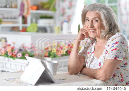 Portrait of beautiful senior woman using modern tablet while drinking tea Portrait of beautiful senior woman using modern tablet while drinking tea 114844040