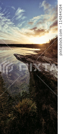The tranquil lake reflects a scenic sunset, creating a serene and beautiful landscape 114844164