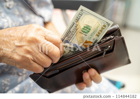Asian senior woman holding and counting US dollar banknotes money in purse. Poverty, saving problem in retirement. 114844182