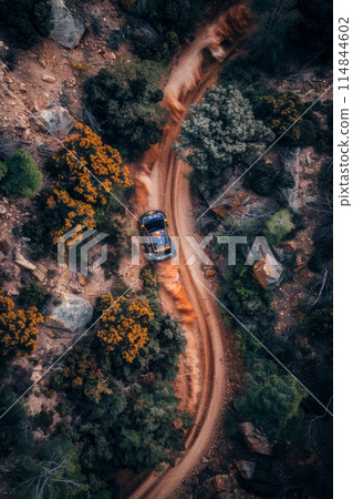 Aerial view of car navigating winding dirt road through rugged landscape. Challenging conditions on way to win. Aerial view of car navigating winding dirt road through rugged landscape. Challenging conditions on way to win. 114844602