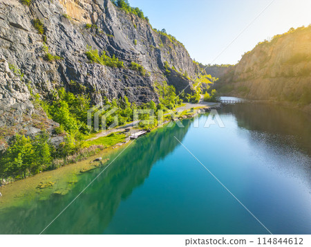 Sunlit limestone cliffs and tranquil water at Velka Amerika quarry in Czechia, captured at sunrise, showcasing the breathtaking natural scenery and geological formations. Sunlit limestone cliffs and tranquil water at Velka Amerika quarry in Czechia, captured at sunrise, showcasing the breathtaking natural scenery and geological formations. 114844612