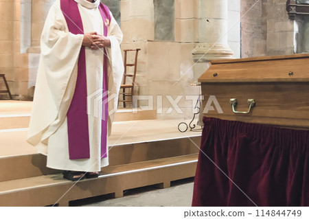 A priest in a church cassock conducts a funeral service in a French church A priest in a church cassock conducts a funeral service in a French church 114844749