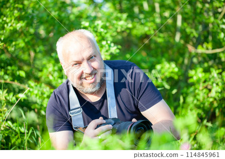 A mature man photographer capturing moments outdoors with his professional camera amidst greenery 114845961