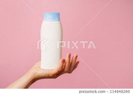 Woman Hand holding white bottle of shampoo or hair conditioner on pink background Woman Hand holding white bottle of shampoo or hair conditioner on pink background 114848260