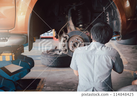 Car service, repair and maintenance concept - auto mechanic man changing tire in auto repair shop. 114848425