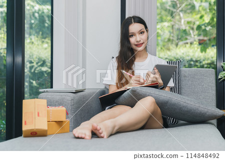 Successful entrepreneur business woman with online sales and Parcel shipping in her home office. Woman checking order on digital tablet. 114848492